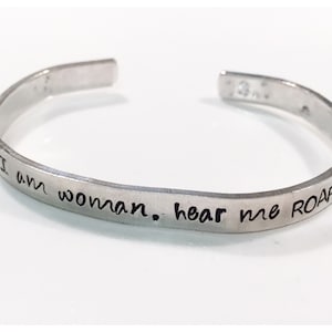 May include: Silver bangle bracelet with the inscription "I am woman. Hear me ROAR!"