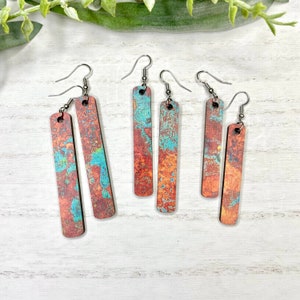 Puede incluir: Conjunto de cuatro pendientes de madera con un diseño abstracto colorido. Los pendientes son de forma rectangular y tienen ganchos plateados.
