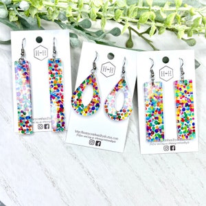 Op de afbeelding: Drie paar kleurrijke confetti-oorbellen. De oorbellen zijn gemaakt van helder hars met een confetti-patroon. De oorbellen zijn verkrijgbaar in drie verschillende vormen: een rechthoek, een traan en een traan met een gat in het midden.