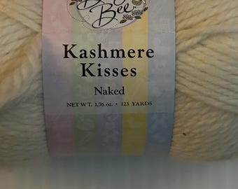 May include: A skein of off-white yarn with a label that reads "Baby Bee Kashmere Kisses Naked." The label has a pastel color scheme with the text "NET WT. 1.76 oz. • 123 YARDS."