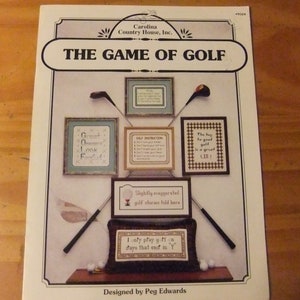May include: A cross-stitch pattern booklet titled "The Game of Golf" with illustrations of golf-themed cross-stitch designs. The designs include phrases like "Great Game Look Fantastic", "Self Instruction", and "The key to good golf is a great lie!"