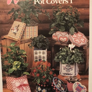May include: Plastic canvas patterns for plant pot covers. The patterns include a house, a heart, a floral design, and a plaid design. The patterns are shown on finished pot covers.