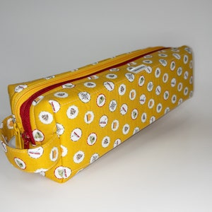 Könnte beinhalten: Eine gelbe Reißverschlusstasche mit einem roten Reißverschluss und einem Griff. Die Tasche hat ein sich wiederholendes Muster aus kleinen weißen Kreisen mit Camping-Motiven darin.