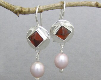 May include: Silver dangle earrings with a red gemstone set in a square shape and a pink pearl drop.