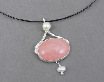 Puede incluir: Un collar de plata con un colgante de piedra preciosa rosa y dos perlas blancas. El collar está en un cordón negro.