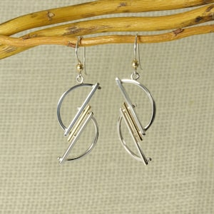 Op de afbeelding: Een paar geometrische oorbellen van zilver en goud met een halve cirkelvorm.