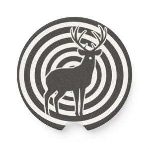 May include: A round, black and white coaster featuring a deer silhouette in the center. The deer is set against a series of concentric circles. The coaster has a small notch on one side.