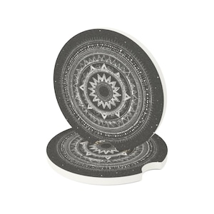 Puede incluir: Dos posavasos redondos para coche con un diseño de mandala en blanco y negro. Los posavasos tienen un borde blanco y una pequeña muesca para facilitar la extracción. El diseño del mandala presenta intrincados patrones geométricos.