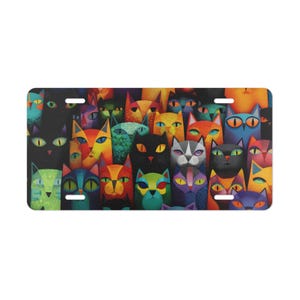 May include: A license plate featuring a colorful, artistic design of numerous stylized cat faces. The cats have various eye colors and fur patterns, with a vibrant palette of orange, blue, green, and purple against a dark background.
