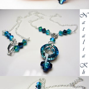 May include: A silver chain necklace with a blue crystal pendant shaped like the female symbol. The crystal is iridescent and has a gradient of blue shades.