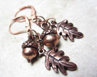 May include: Copper-toned earrings featuring acorn and oak leaf charms. The earrings have a lever-back closure. The acorn charms have detailed caps and the oak leaf charms have intricate veining. The earrings are designed with a rustic, nature-inspired aesthetic.