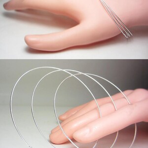 May include: A set of three silver-colored, thin, wire-like bangles. The bangles are circular and appear to be made of a shiny metal. The image shows the bangles on a hand, suggesting they are jewelry.