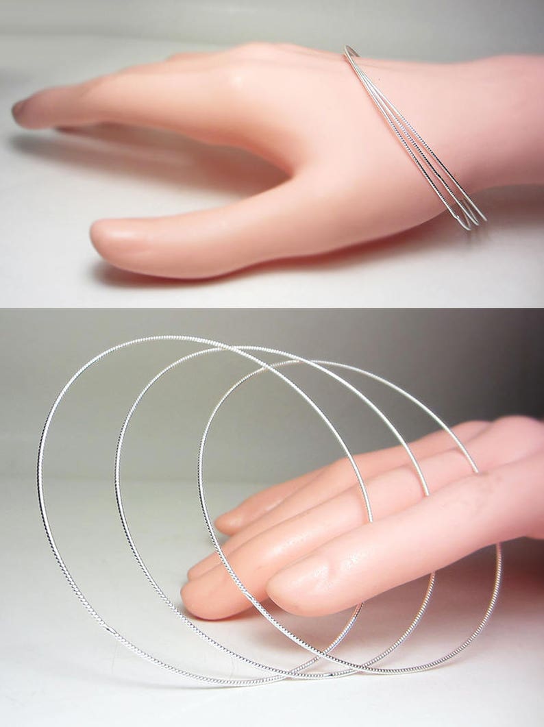 May include: A set of three silver-colored, thin, wire-like bangles. The bangles are circular and appear to be made of a shiny metal. The image shows the bangles on a hand, suggesting they are jewelry.