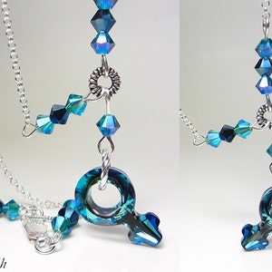May include: A silver chain necklace with a blue crystal pendant in the shape of the female gender symbol. The pendant is surrounded by smaller blue crystals.