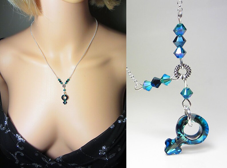 May include: A silver chain necklace with a dark green crystal pendant in the shape of the female symbol. The necklace is adorned with smaller dark green crystals.
