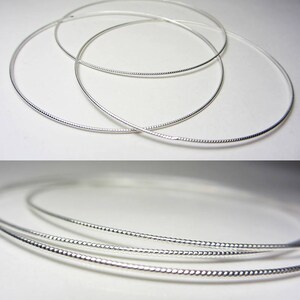 May include: Several silver-colored necklaces with a textured design are displayed against a white background. The necklaces are circular and appear to be made of a thin, flexible metal. The image is well-lit, highlighting the reflective quality of the jewelry.