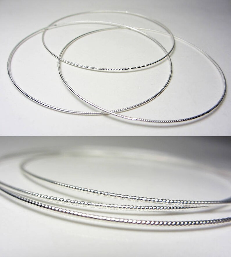 May include: Several silver-colored necklaces with a textured design are displayed against a white background. The necklaces are circular and appear to be made of a thin, flexible metal. The image is well-lit, highlighting the reflective quality of the jewelry.