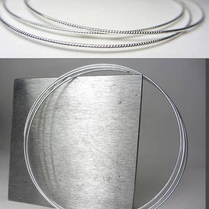 May include: Three silver-colored necklaces with a twisted rope design. The necklaces are circular and appear to be made of a shiny metal. The image is well-lit, highlighting the texture and shape of the jewelry.