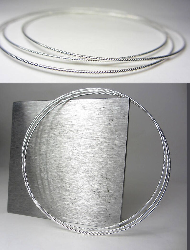 May include: Three silver-colored necklaces with a twisted rope design. The necklaces are circular and appear to be made of a shiny metal. The image is well-lit, highlighting the texture and shape of the jewelry.