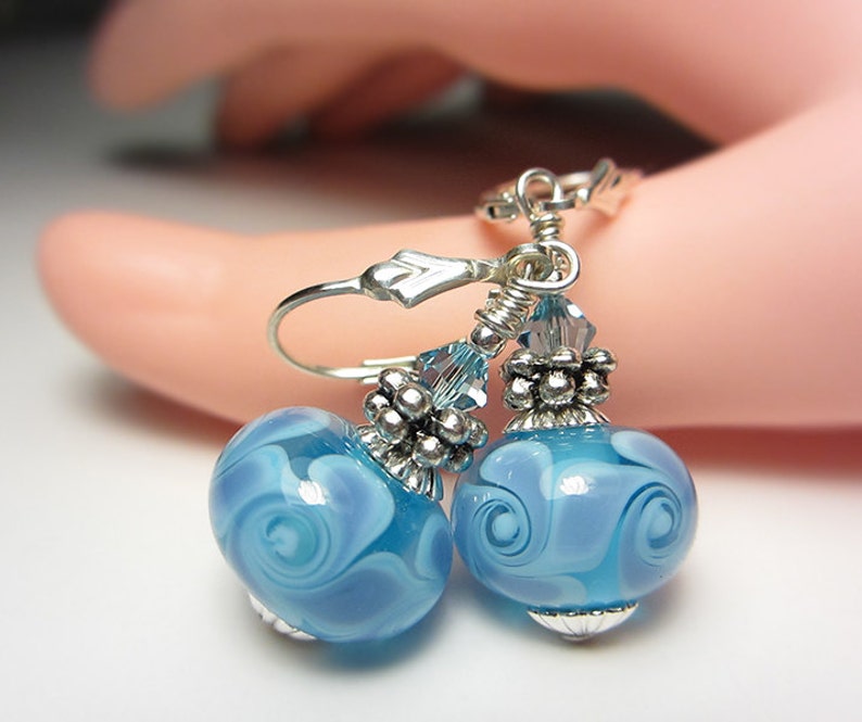 Pu&ograve; includere: Orecchini pendenti con perline di vetro azzurro chiaro e motivi a spirale bianchi. Hanno dettagli in metallo argentato e chiusure a leva. Le perline misurano circa 2 cm di diametro.
