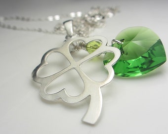 Puede incluir: Collar plateado con un colgante de trébol de cuatro hojas y un charm en forma de corazón verde. La cadena es fina y brillante. El colgante de trébol es detallado y el corazón es de un verde vibrante.