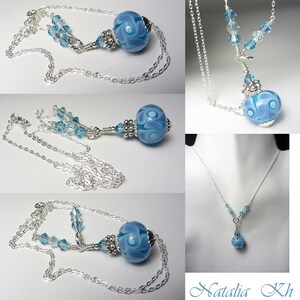 May include: A silver necklace featuring a large, round, light blue glass bead with a swirling design. The bead is connected to the chain with smaller blue crystal accents. The necklace is displayed in multiple views.