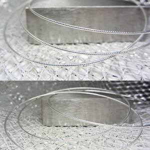 May include: Close-up of several silver-colored necklaces with a delicate, twisted design. The necklaces are arranged in a circular shape, resting on a textured, metallic surface. The image highlights the intricate details of the jewelry.