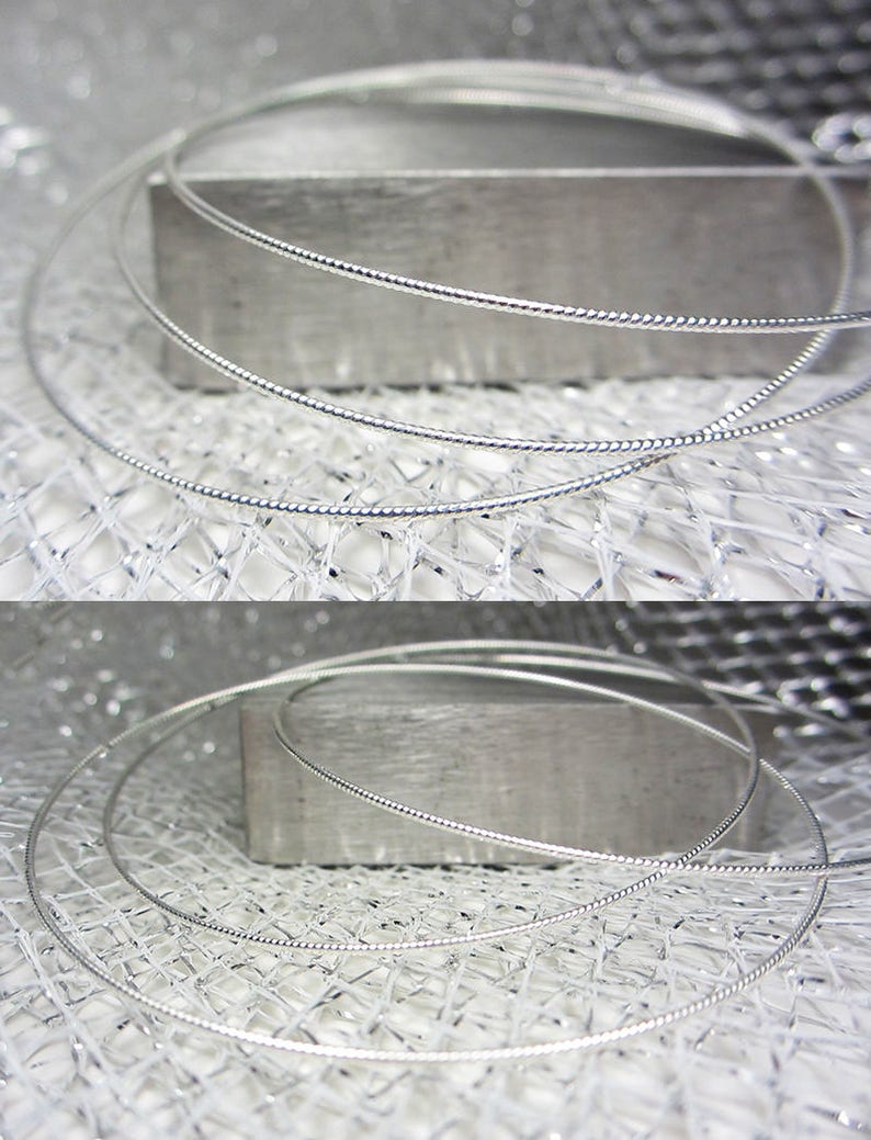 May include: Close-up of several silver-colored necklaces with a delicate, twisted design. The necklaces are arranged in a circular shape, resting on a textured, metallic surface. The image highlights the intricate details of the jewelry.