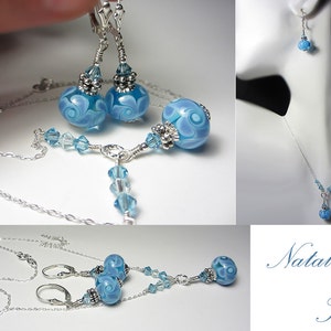 May include: A jewelry set featuring a necklace and earrings. The set includes a silver chain necklace with a blue glass bead pendant and matching earrings. The earrings and pendant have a swirl design. The set is displayed on a white background.