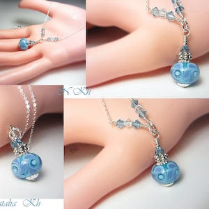 May include: A delicate silver necklace featuring a pendant with a blue and white swirled glass bead. The pendant is accented with small blue crystals and silver detailing. The necklace is displayed on a light background.