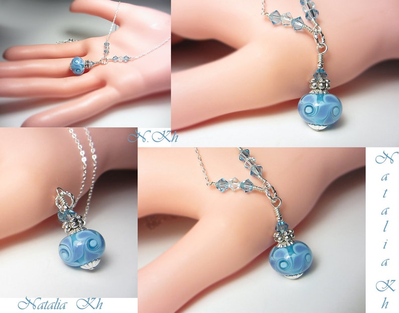 May include: A delicate silver necklace featuring a pendant with a blue and white swirled glass bead. The pendant is accented with small blue crystals and silver detailing. The necklace is displayed on a light background.