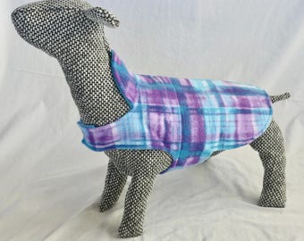 May include: A dog coat in a blue and purple plaid pattern. The coat is made of a soft material and is designed to fit a dog. The dog form is covered in a black and white speckled fabric.