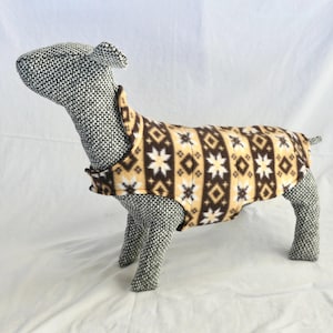 May include: A dog sweater with a geometric pattern in brown, white, and tan. The sweater has a high collar and a sleeveless design, perfect for keeping a small dog warm. The pattern includes diamonds and star-like shapes.
