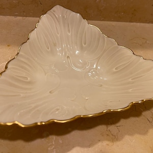 May include: A white porcelain triangular dish with a gold rim and a decorative floral design.