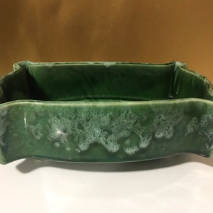May include: A green ceramic planter with a unique, wavy design. The planter has a mottled green glaze with white flecks.