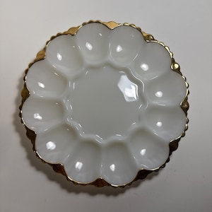 Peut inclure: Un plat à œufs blanc et festonné avec un bord doré. Le plat comporte une zone centrale et douze sections individuelles pour les œufs. Le plat est fait d'un matériau brillant et est conçu pour servir des œufs.