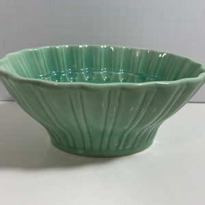 Puede incluir: Un cuenco de cerámica verde claro con un borde festoneado y nervaduras verticales. El cuenco está hecho en un estilo clásico y tiene un acabado liso y brillante.