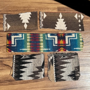 May include: A collection of woven fabric samples with geometric patterns. The samples feature designs in brown, white, blue, green, red, and black. The fabrics have a textured appearance and are arranged on a wooden surface.