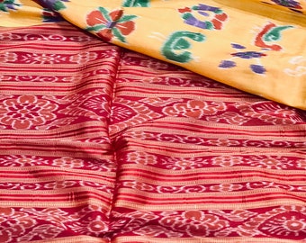 May include: A red and white patterned fabric with a yellow and green patterned fabric folded on top. The fabric has a traditional ikat design.