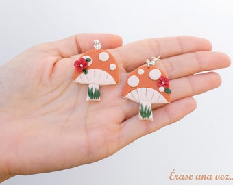 May include: A pair of mushroom-shaped earrings with white and orange accents. Each earring features a red flower and green leaves.