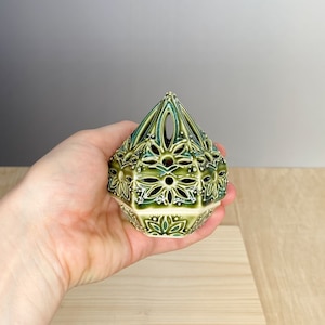 Op de afbeelding: Een groene en witte keramische wierookbrander met een geometrisch ontwerp. De brander is piramidevormig met ingewikkelde bloemmotieven.