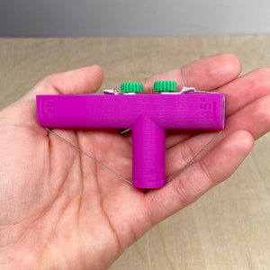 May include: A pink plastic T-shaped tool with two green knobs and markings for 30, 45, and 49 degrees. The tool is used for creating angles in woodworking.
