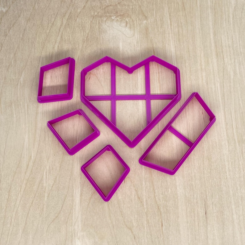 May include: A set of five pink plastic cookie cutters in the shape of a heart, a square, and three diamonds.