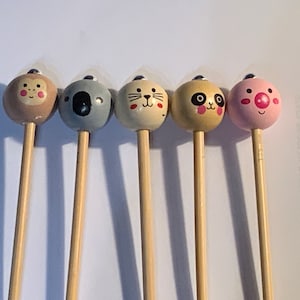 May include: Six wooden sticks with animal faces on the top. The animals are a monkey, a koala, a cat, a panda, and a pig. The sticks are all the same length and are made of natural wood.