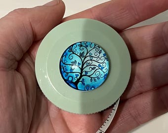 May include: A light green retractable tape measure with a blue and white tree of life design on the front.