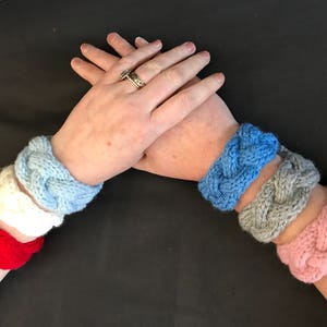 May include: Four knitted bracelets in different colors: red, white, blue, and pink. The bracelets are braided and have a simple design.