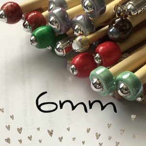 May include: A set of 6 mm knitting needles with colourful, decorative beads on the ends. The needles are made of wood and have a natural finish.