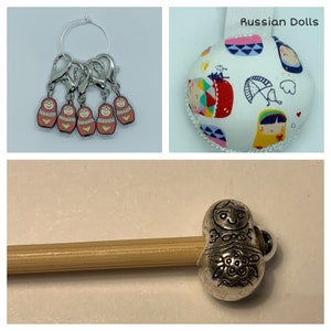May include: A set of six silver and pink Russian doll stitch markers, a white pincushion with a Russian doll design, and a silver Russian doll stitch marker on a wooden knitting needle.