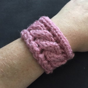 May include: A pink knitted bracelet with a cable knit pattern.