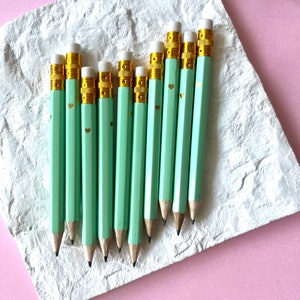 Op de afbeelding: Een set van tien mintgroene potloden met gouden accenten en witte gummen. Elk potlood heeft een klein gouden hartontwerp.